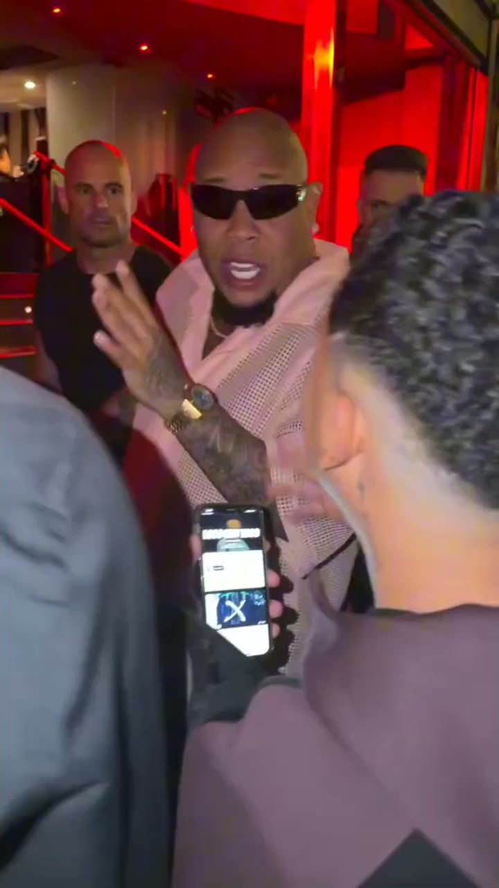 Bulin 47 in sunglasses freestyling at a red-lit venue entrance while a fan holds up a phone
