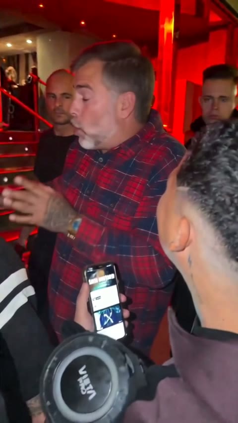 A dad with salt-and-pepper hair and a gray beard in a flannel shirt at the red-lit entrance, the crowd behind
