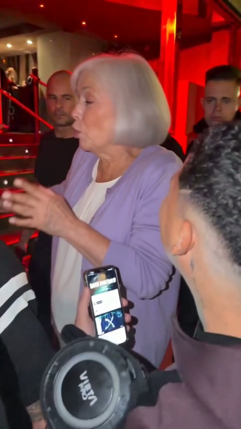 A grandmother with a short white bob and a lavender cardigan freestyling beside the man with the speaker